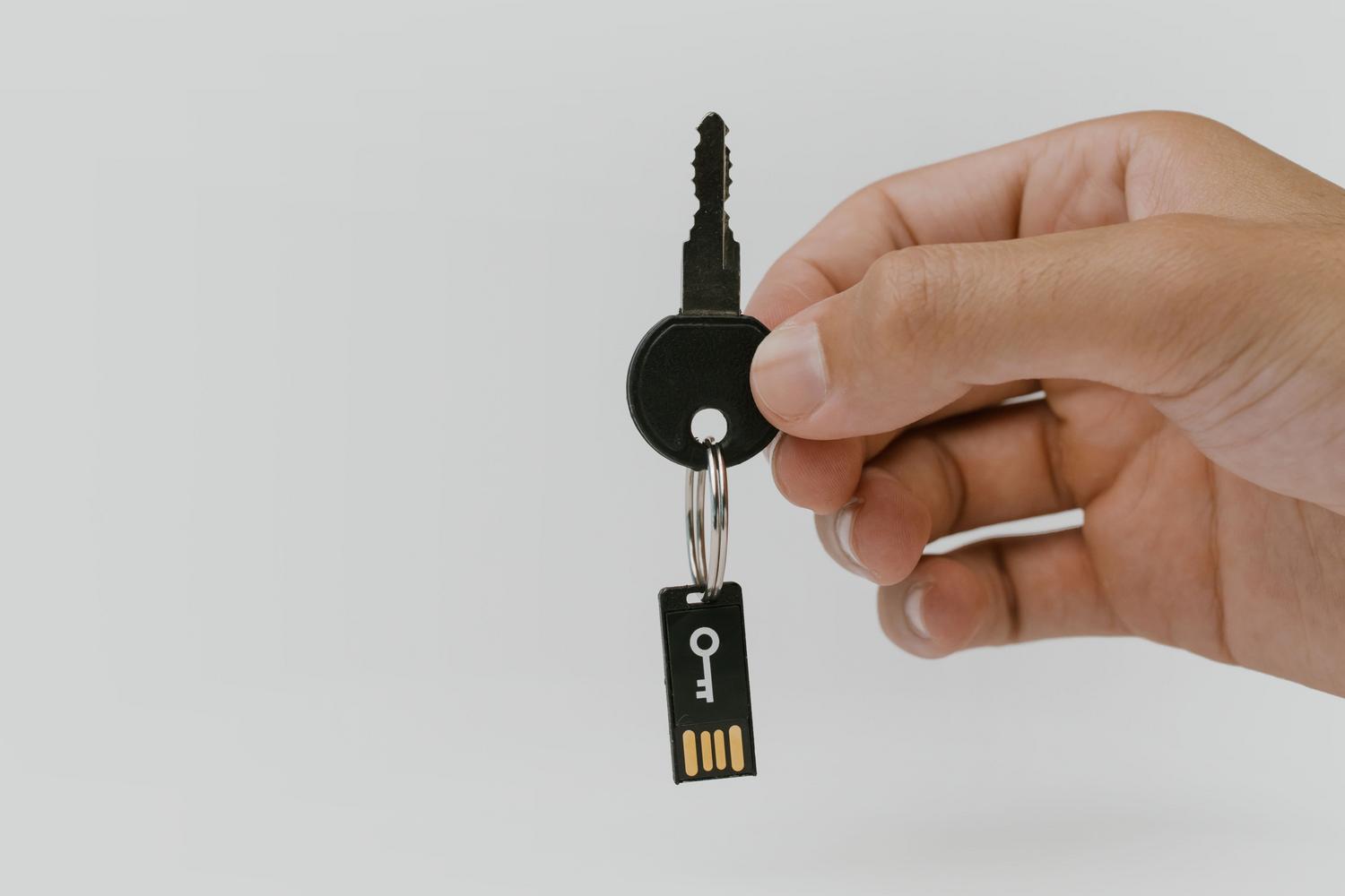 يد تحمل مفتاحًا ماديًا وذاكرة فلاش USB، ترمز بشكل مفاهيمي إلى التشفير وحماية البيانات الحساسة.